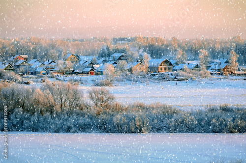 Christmas snowy landscape scene with wooden houses under light falling snow. Birds eye view of winter countryside at Christmas Eve