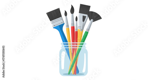 An assortment of art brushes are held upright in a clear glass jar.
