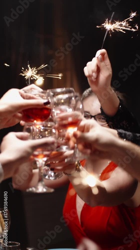 Vertical cinematic slow motion video joyful friends raising glasses with sparklers at festive dinner table cozy warm light holiday atmosphere concept friendship celebration christmas new year