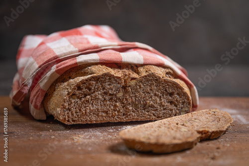 Sliced whole grain walnut bread wrapped in checkered kitchen cloth
