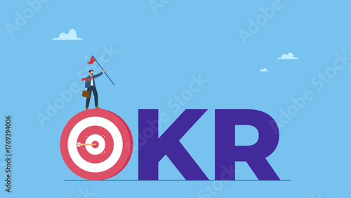 Businessman holding winning flag on target with the work OKR. OKR, objective and key result framework to measure success and improvement, goal setting or define measurable target for business.