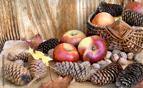 bright red apples, walnuts pine cones and autumnal leaf with wiker basket bac...