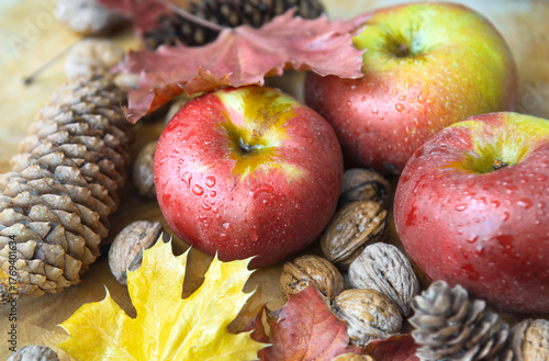 closeup on bright red apples covered by drops, walnuts and pine cones on a pl...