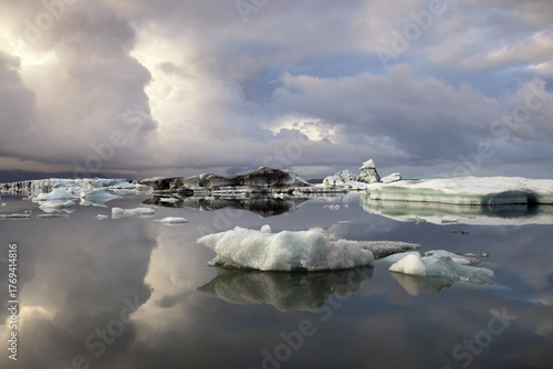 View of luminous icebergs drift silently on the glacial lagoon beneath a dramatic sky mirroring the serene waters, Jokulsarlon, Sveitarfélagio Hornafjorour, Iceland.
