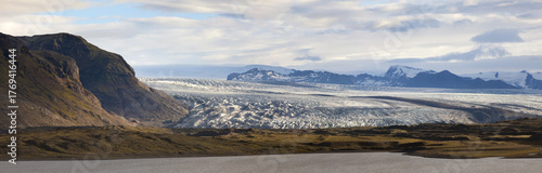 View of a vast glacial expanse meeting rugged mountains and placid waters under a serene sky, Jokulsarlon, SveitarfÃ©lagiÃ° HornafjÃ¶rÃ°ur, Iceland.