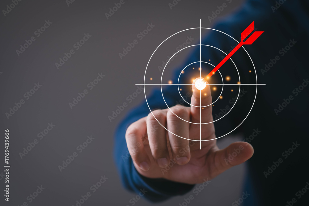 Obraz premium Close-up of a hand touching a digital target with a red arrow hitting the center. Concept of goal setting, success strategy, business planning, achievement, focus, and performance optimization.