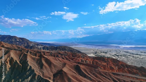 Bright hot sun dazzles the barren desert among the mountain ranges. Drone flight over the Death Valley National Park, California, USA.