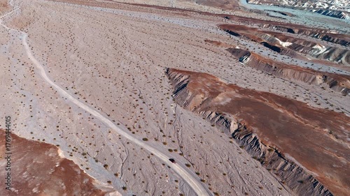Approaching a red car standing on the road crossing the desert. View on the barren Death Valley National Park, California, USA. From drone.