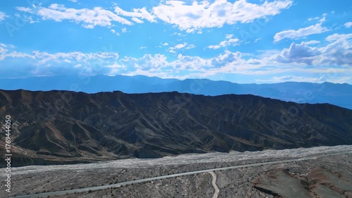 Dark ridged rocks with no vegetation. Blue sky with clouds at backdrop. Rising over the Death Valley National Park, California, USA.