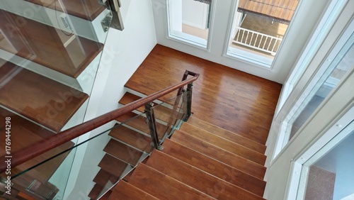 A modern wooden staircase with glass railing in a bright home interior. Clean, elegant design with natural light from large windows. Suitable for interior design, architecture, and home decor concepts