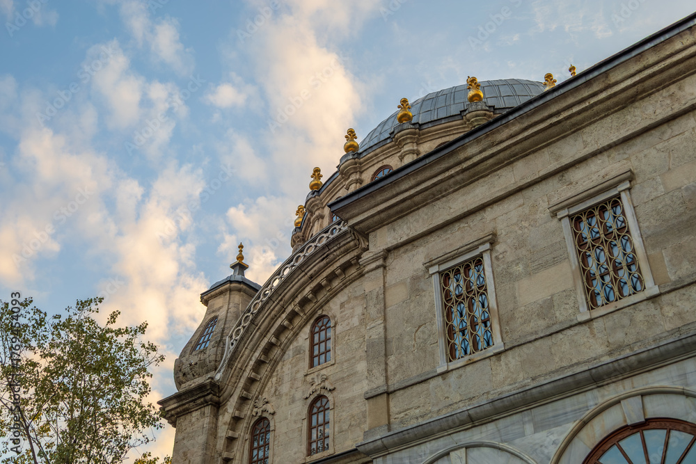 Fototapeta premium Low-angle close-up of a historic Nusretiye mosque's stone facade and gilded dome against a cloudy sky