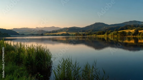 Lake reflecting hills and golden sky at sunset, reeds growing along the tranquil water's edge