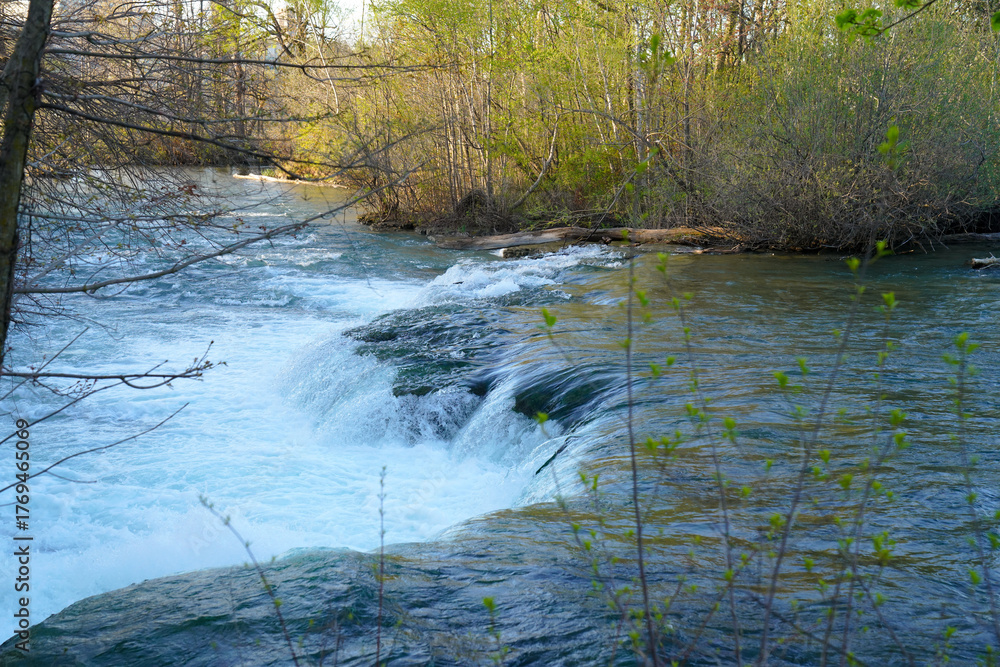 Obraz premium A serene view of a small cascade along the Niagara River in New York, surrounded by spring foliage and gentle light reflecting off the flowing water.