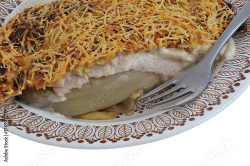 Assiette d'endive au jambon gratinée maison avec une fourchette en gros plan sur fond blanc