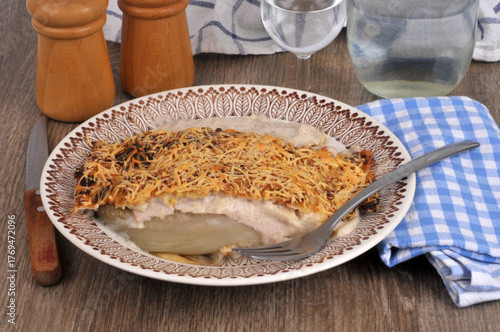 Assiette d'endive au jambon gratinée maison avec une fourchette et une verre d'eau servie à table