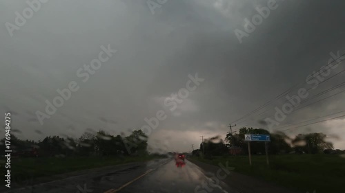 Point of view through a car windshield in a violent rainstorm on a rural highway. Dark sky, blurred headlights and red brake lights on wet asphalt create tension, isolation and end-of-day fatigue.