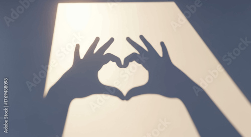 Hands forming a heart shape against a bright light shining through a window with a dark background.