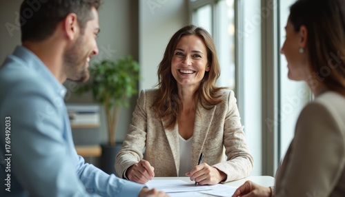 Woman agent smiles while reviewing contract with couple. Man and woman listen intently as papers are signed. Business meeting involves discussion and agreement between parties.