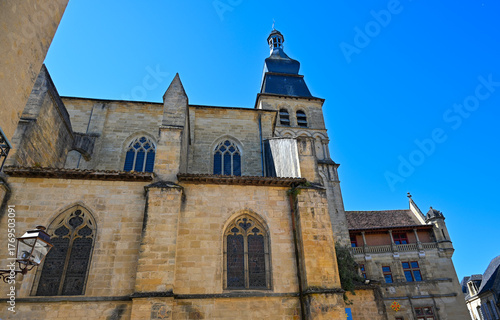 Cathedral Saint-Sacerdos towers over the charming streets of Sarlat in Dordogne, exhibiting its intricate stonework and historical significance against a backdrop of bright blue skies.