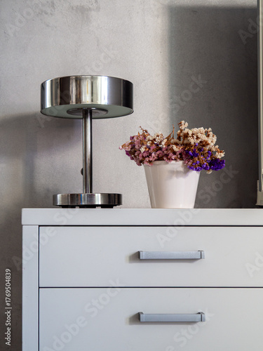 Modern Bedroom Dresser with Metal Lamp and Dried Flower Arrangement. Elegant and minimalist interior design. Nightstand with metallic light and bouquet with copy space. Calm furniture home decor.