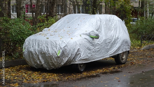 A car parked near the lawn is covered with a new white cover to protect it from the weather
