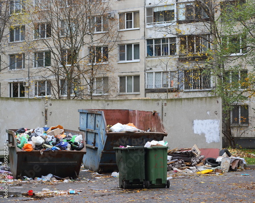 Various garbage containers full of garbage are located in the courtyard of an apartment building