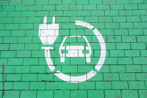 Top view parking space for electric car with green-marked charging station, road markings, white charging symbol on asphalt, urban street infrastructure, modern sustainable transport. 