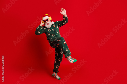 Dancing Santa in festive pajamas wears headphones and striped socks against a bold red background for christmas fun