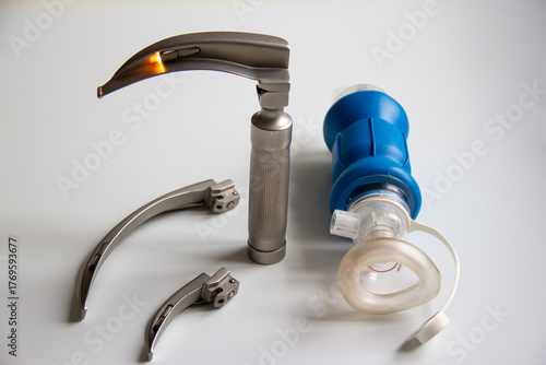 On a white table is a laryngoscope with two blades and a breathing bag for newborns. Horizontal shot.