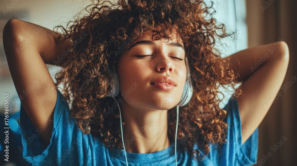 Fototapeta premium A young woman with curly hair listens to music absorbed in a peaceful moment of relaxation.