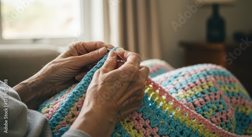 Elderly person's hands actively working on a colorful crocheted blanket indoors