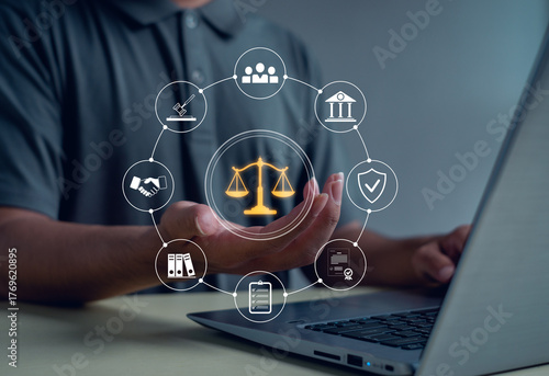 Business person using digital justice scale and law icons above laptop symbolizing legal services, corporate compliance, fairness, protection, and professional consulting in modern technology.
