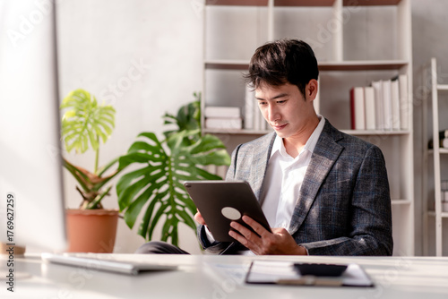 A man in a suit is sitting at a desk with a tablet in front of him