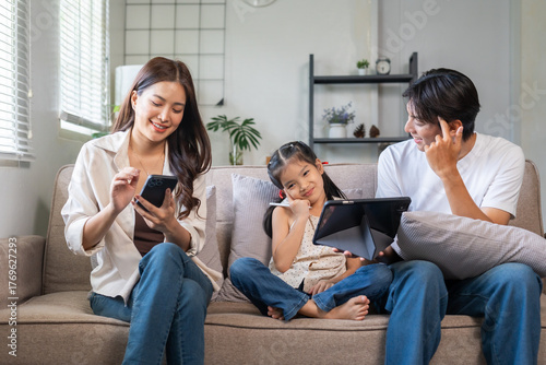 Fotografie Asian family relaxed on sofa, parents and daughter sharing tablet while mother s
