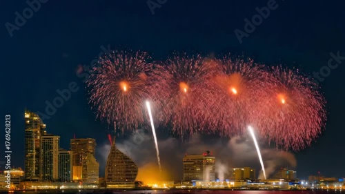 Spectacular red fireworks explode over modern cityscape at night illuminating illuminated