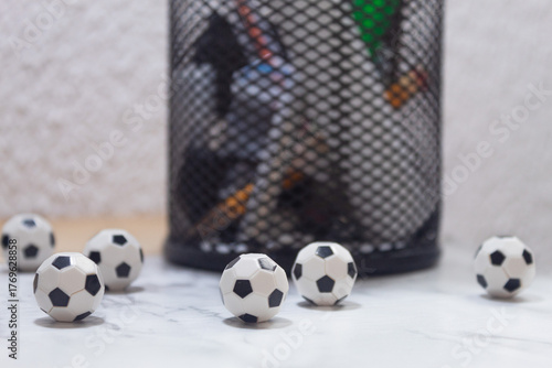 Several small soccer balls next to a metal pencil holder on a desk