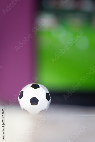 Miniature soccer ball in front of a screen showing a blurred sports match