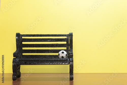 Mini soccer ball placed on a black bench with a solid yellow background