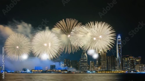 Spectacular pink fireworks explode over a modern city skyline at night reflecting on the water