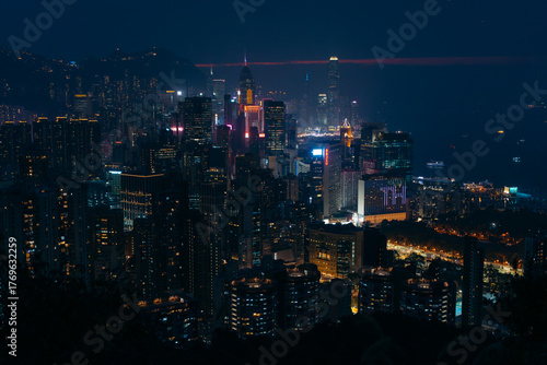 Aerial view of a vibrant metropolis where a symphony of illuminated skyscrapers pierce the dark sky, reflecting on the tranquil harbor waters, Hong Kong, Hong Kong.