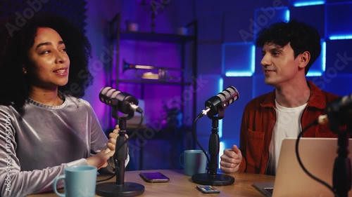 Female radio anchor talking with male colleague, recording show in studio