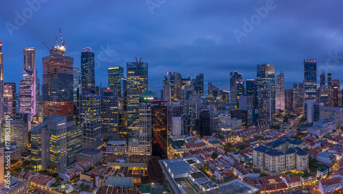 Aerial view of a glittering cityscape where towering skyscrapers pierce the twilight sky, their lights reflecting off the dark waters of Marina Bay, Singapore, Singapore.