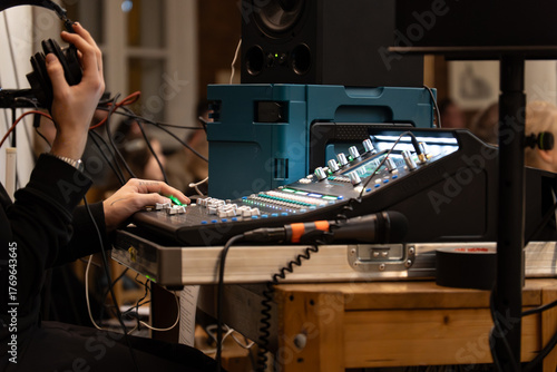 Sound engineer operating professional audio mixing console during live concert or event – adjusting sound levels with headphones in studio or venue