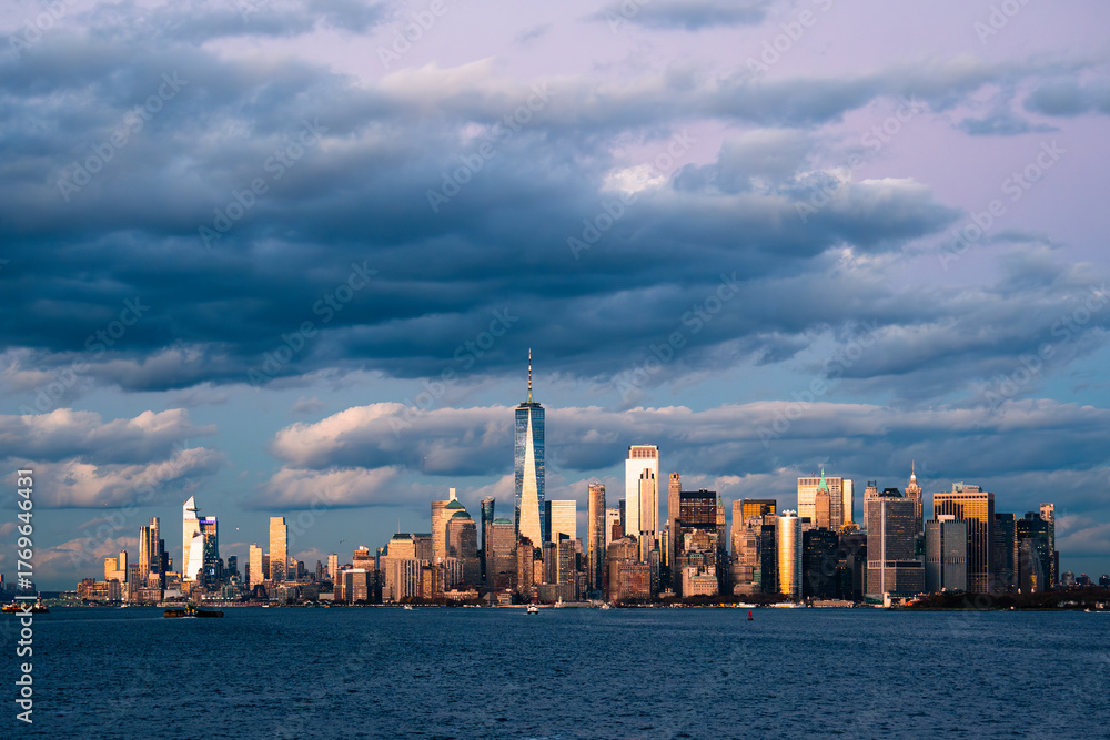© Travel 'n' Lifestyle - View of a sprawling cityscape kissed by the warm glow of the setting sun, set against a backdrop of dramatic, swirling clouds, New York, New York, United States.