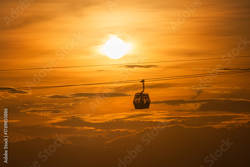 Cable car at sunset with the sun behind and orange-hued clouds