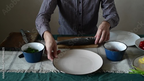 A man begins to cut up a sea bass, cutting off its fins.