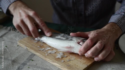 A man cleans fish from scales with a knife