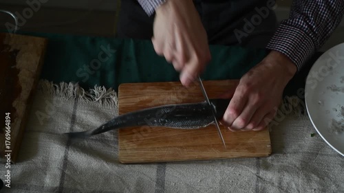 A man guts a sea bass fish with a knife