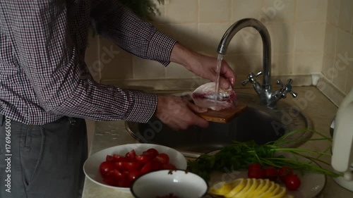A man washes gutted fish with water under the tap.