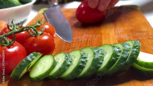 A woman's hand slices a ripe tomato on a wooden board. Slow motion.